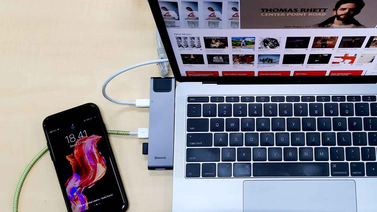 A silver laptop with an USB hub to its side and a smartphone.