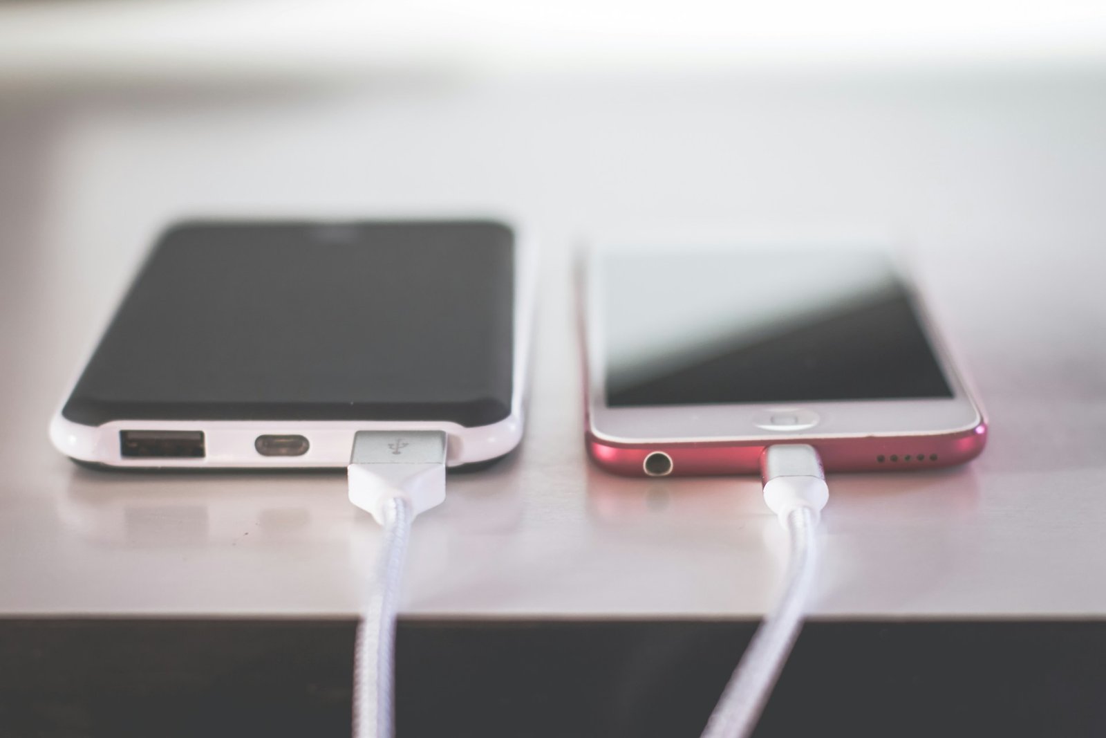 2 Phones getting charged while lying on a desk.