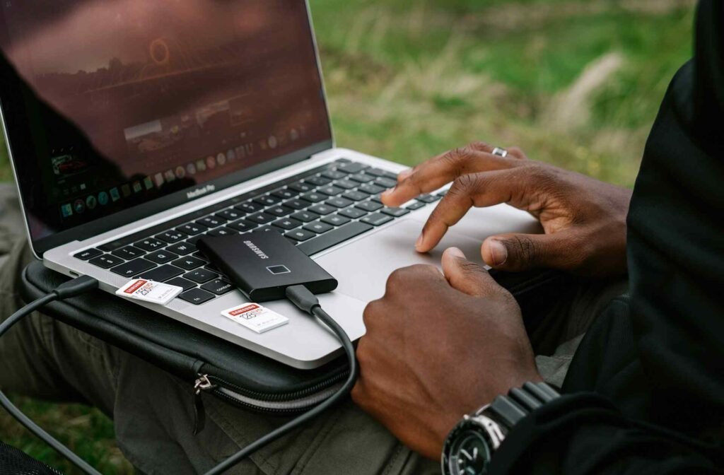 A person using a laptop with an external ssd outside.