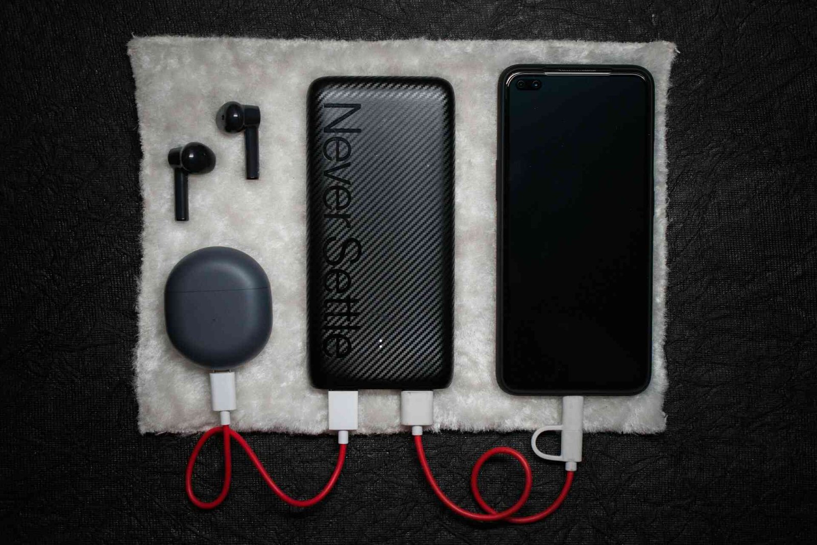 A black powerbank connected to an air pod charger and a smartphone.