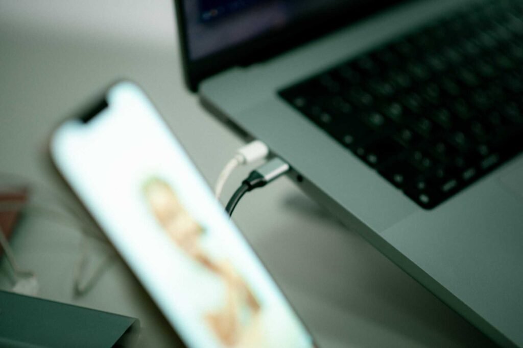 A phone and laptop connected to a USB hub while a person is talking with someone on the phone.