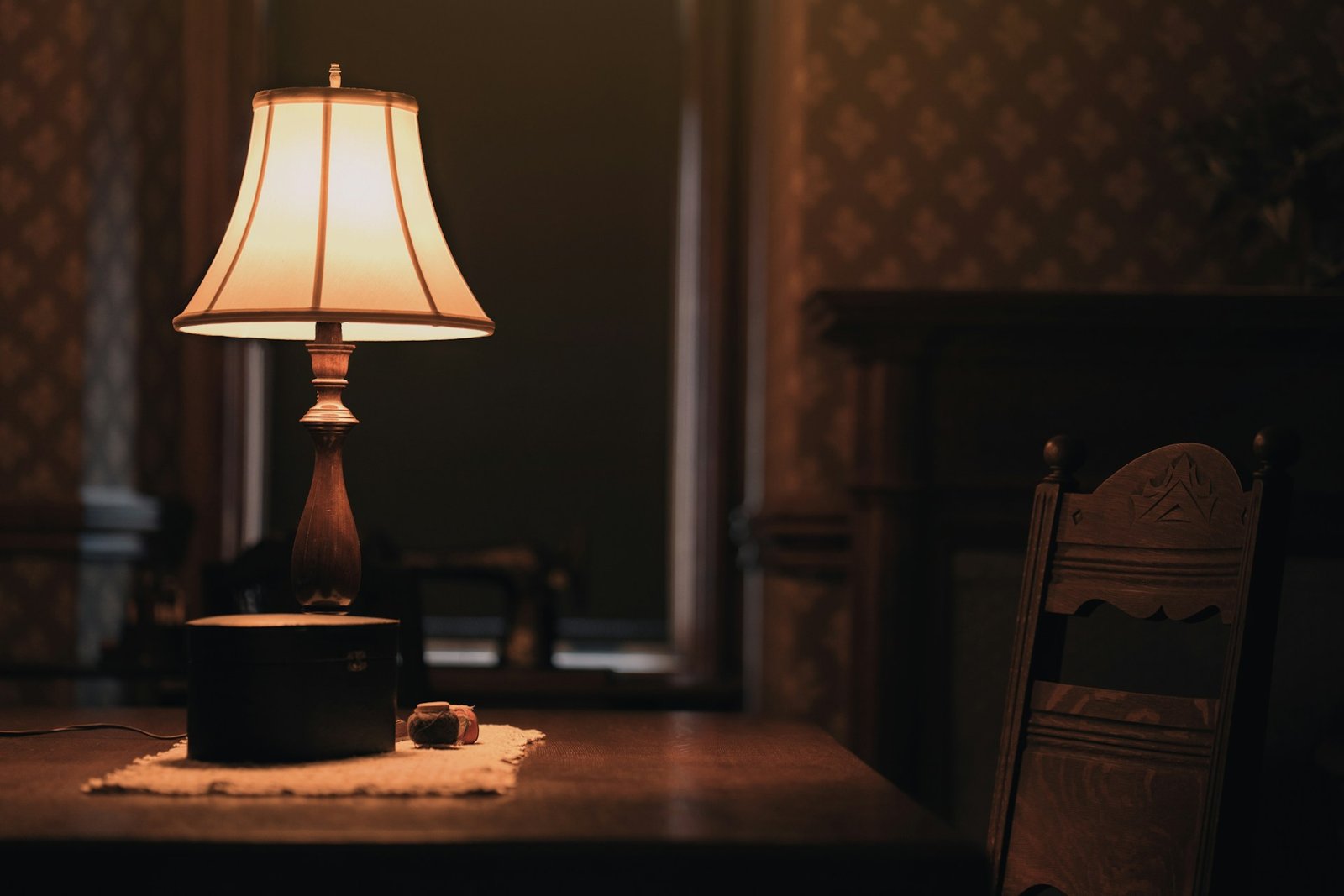A table lamp on a wooden table next to a chair.