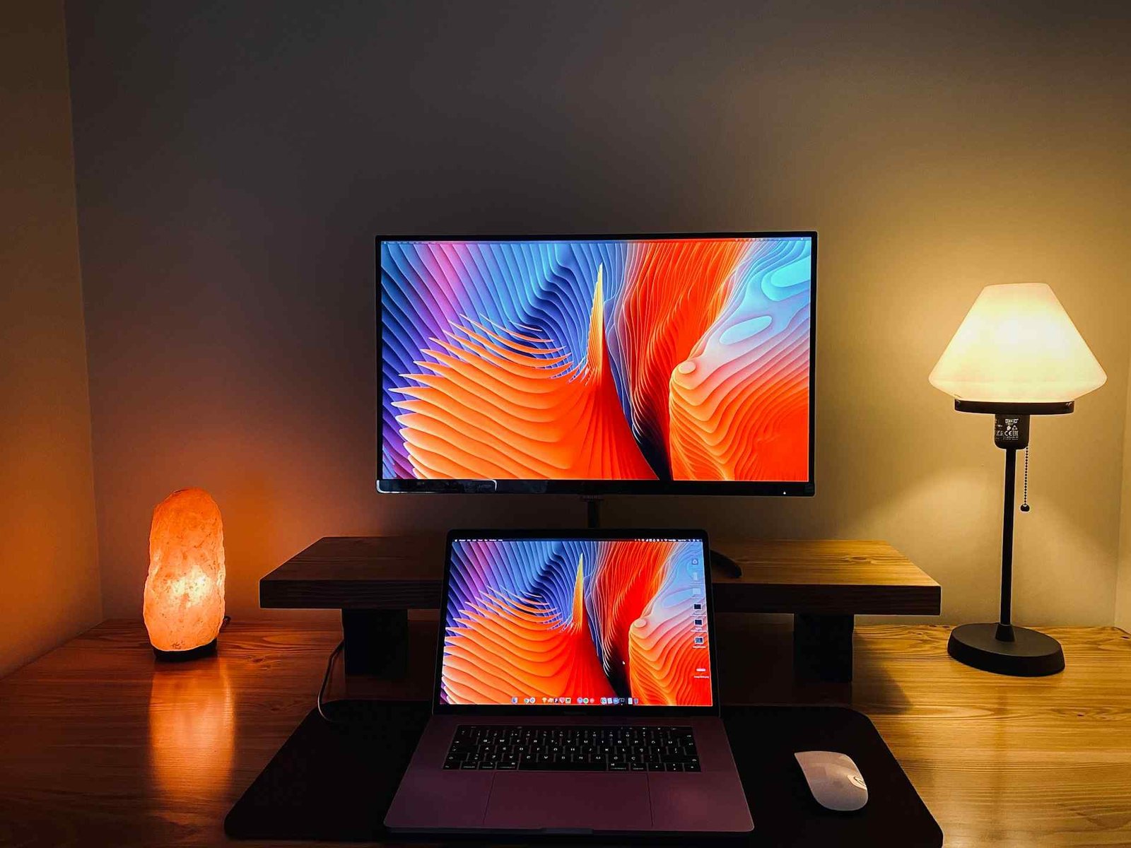 A warm lava lamp light and a slightly cooler lamp light at a workspace with 2 monitors behind each other.