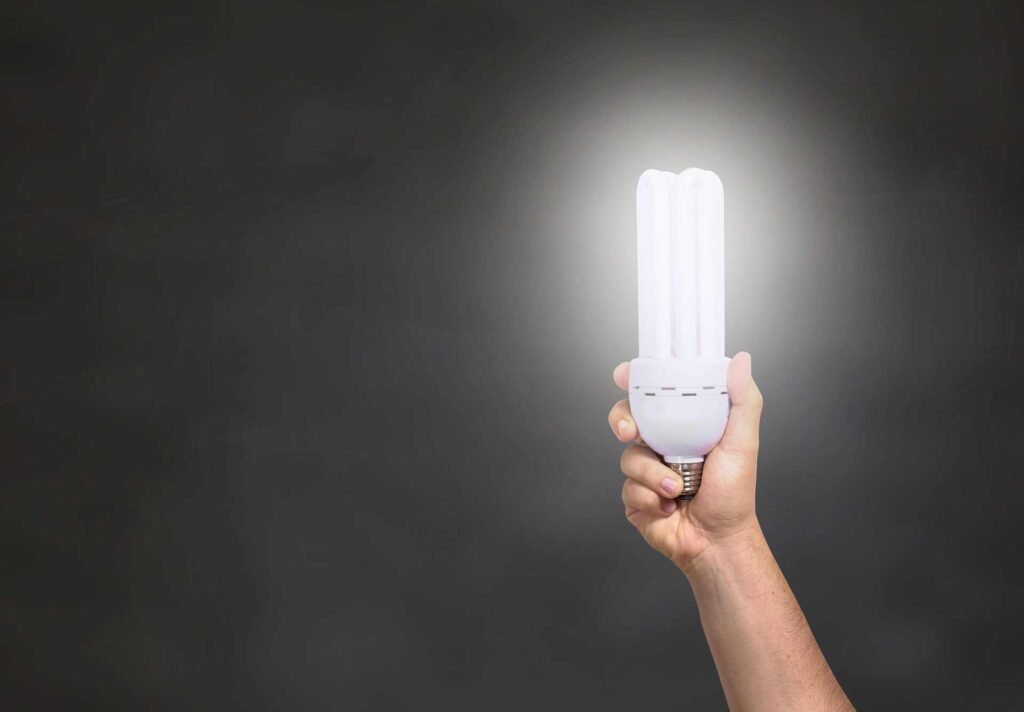 A person holding up a bright white led light into the air on a dark background.