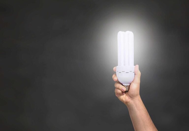 A person holding up a bright white led light into the air on a dark background.