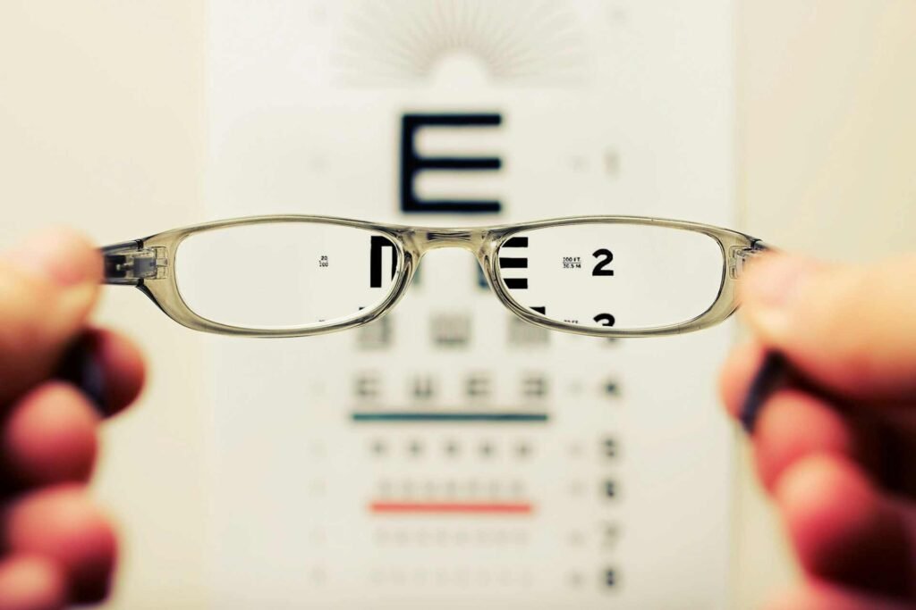 A person holding up glasses in front of a reading table.