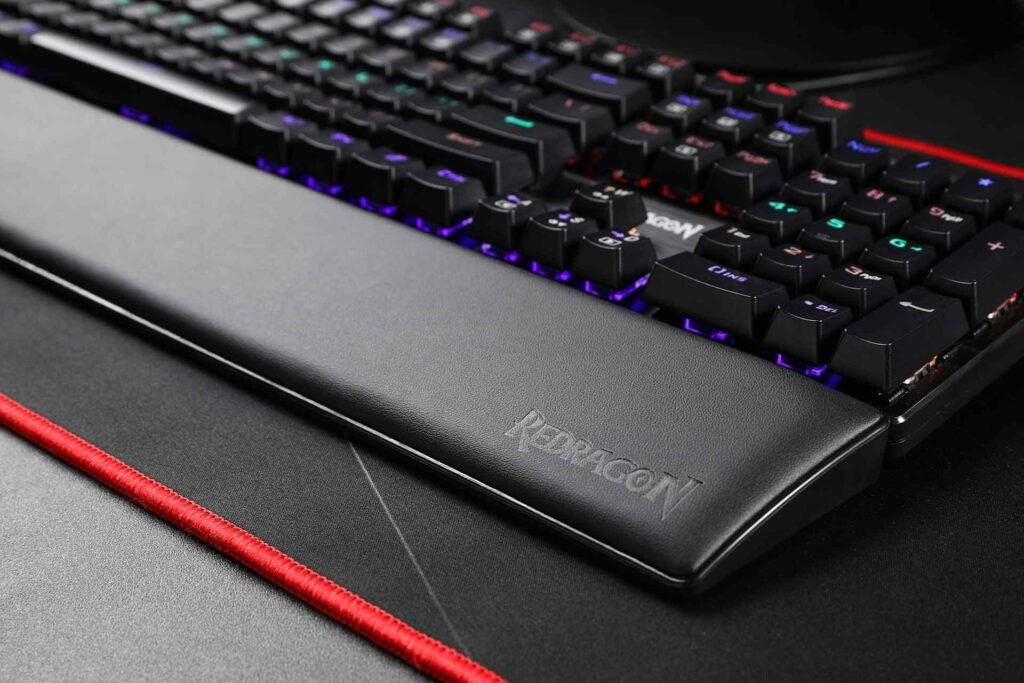 A keyboard wrist rest in front of a mechanical keyboard on a desk mat with a red rim.