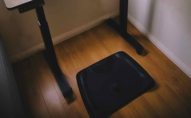 A black balance board below a standing desk on a wooden floor.
