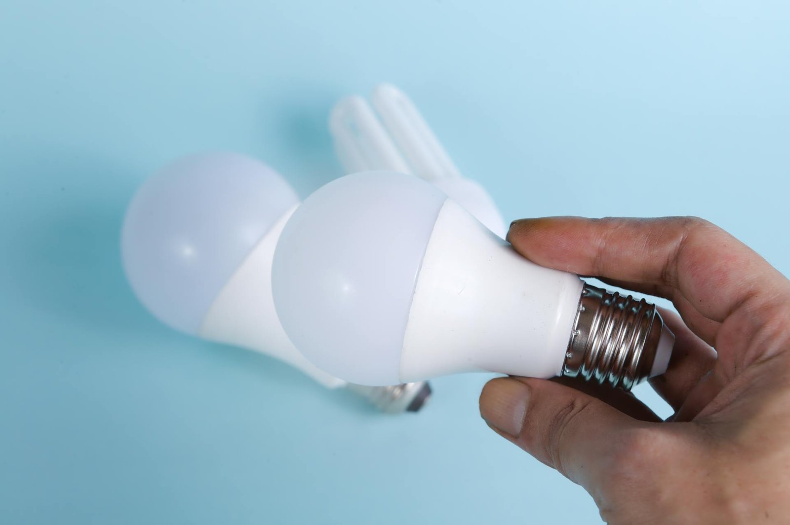 A person holding up an LED light bulb with 2 others laying on the ground behind.