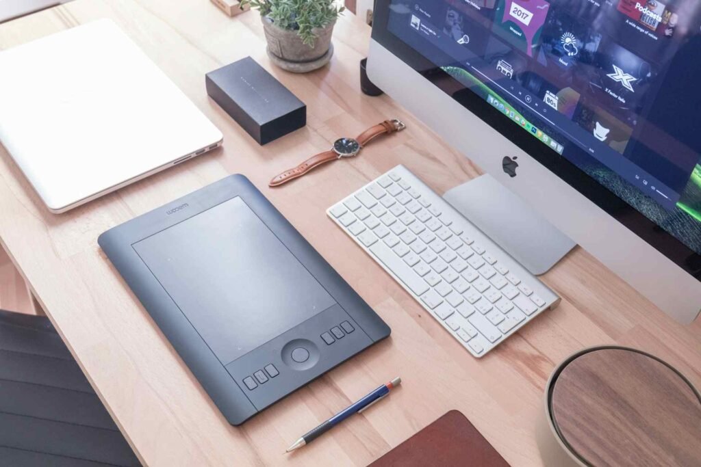 An apple monitor with different productivity tools like a tablet on the wooden table in front of it.