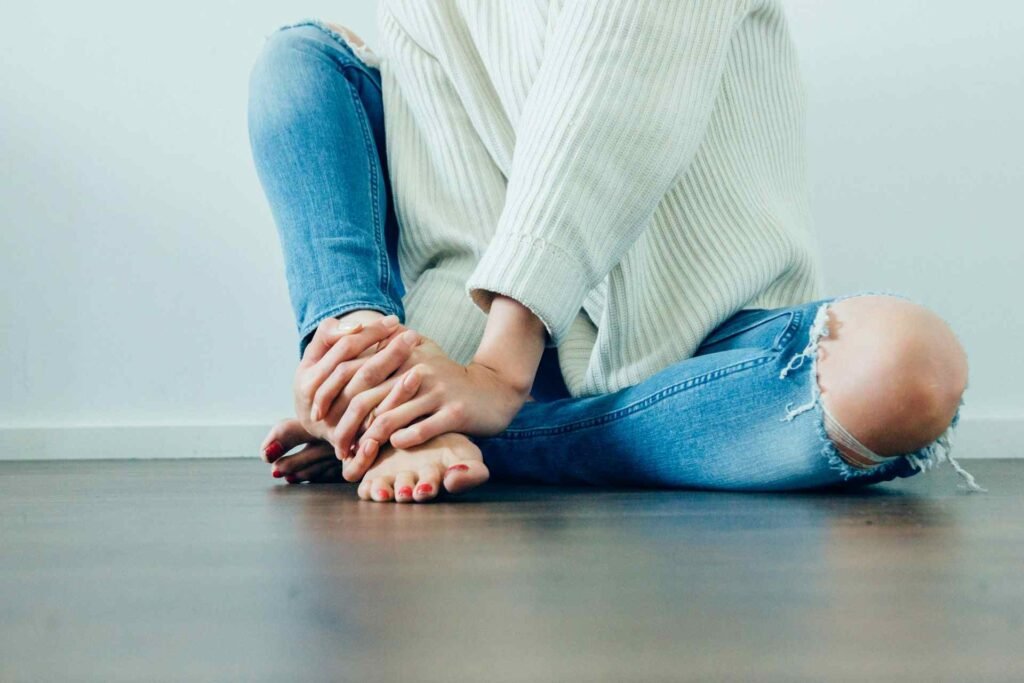 A person wearing blue jeans holding their feet suggesting discomfort.