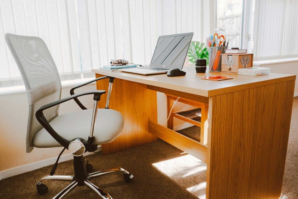 An ergonomic wooden desk setup with a white office chair next to a window.