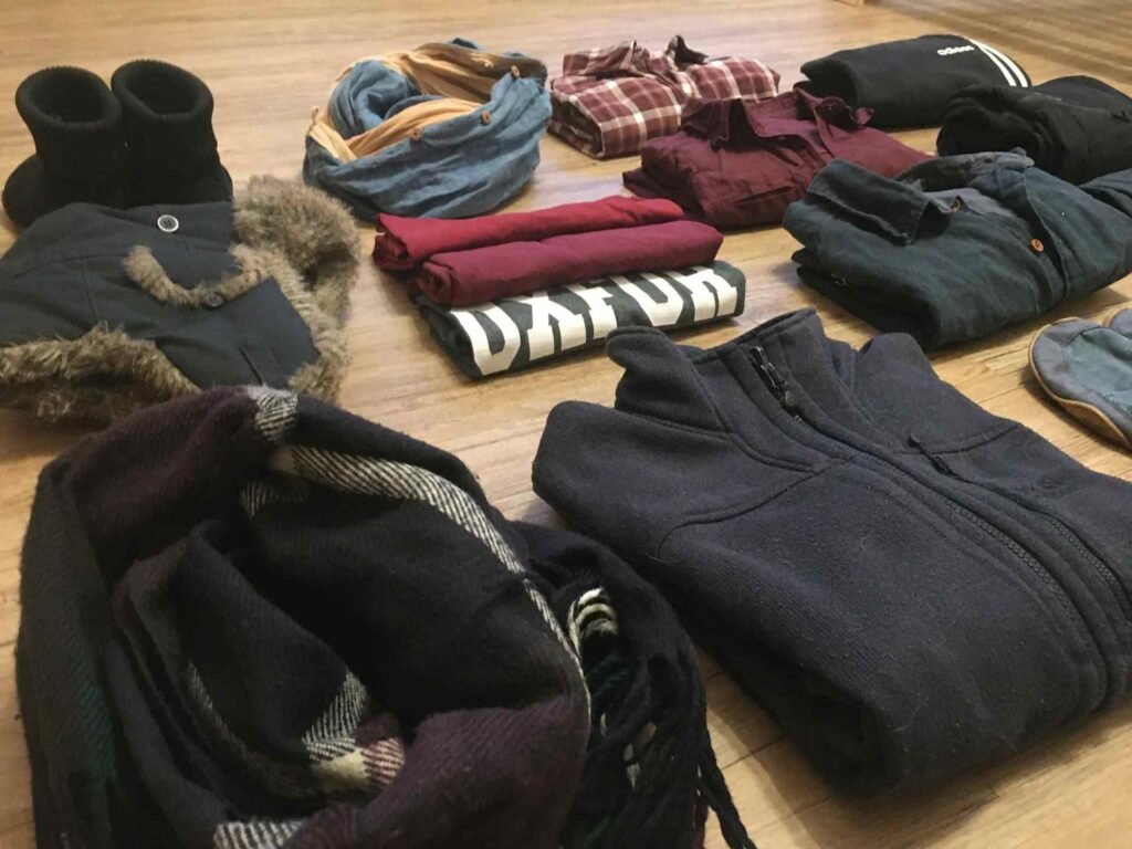 A pile of different warm clothes on a wooden floor.