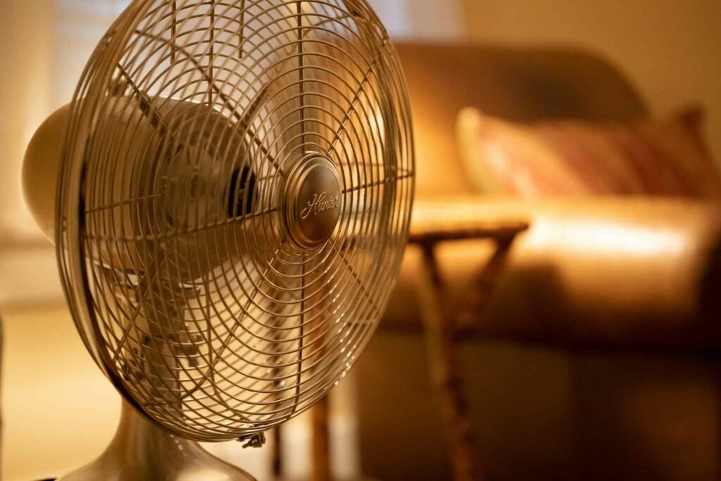 A white fan standing in front of a blurry couch in the background.