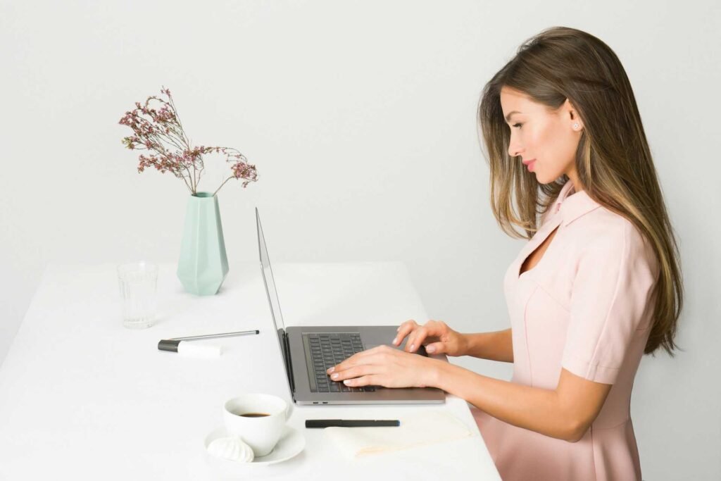 A women wearing pink working on a laptop while sitting with excellent posture.