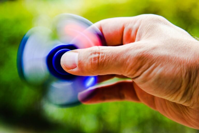 A person spinning a blue fidget spinner in their hand on a blurry green background.