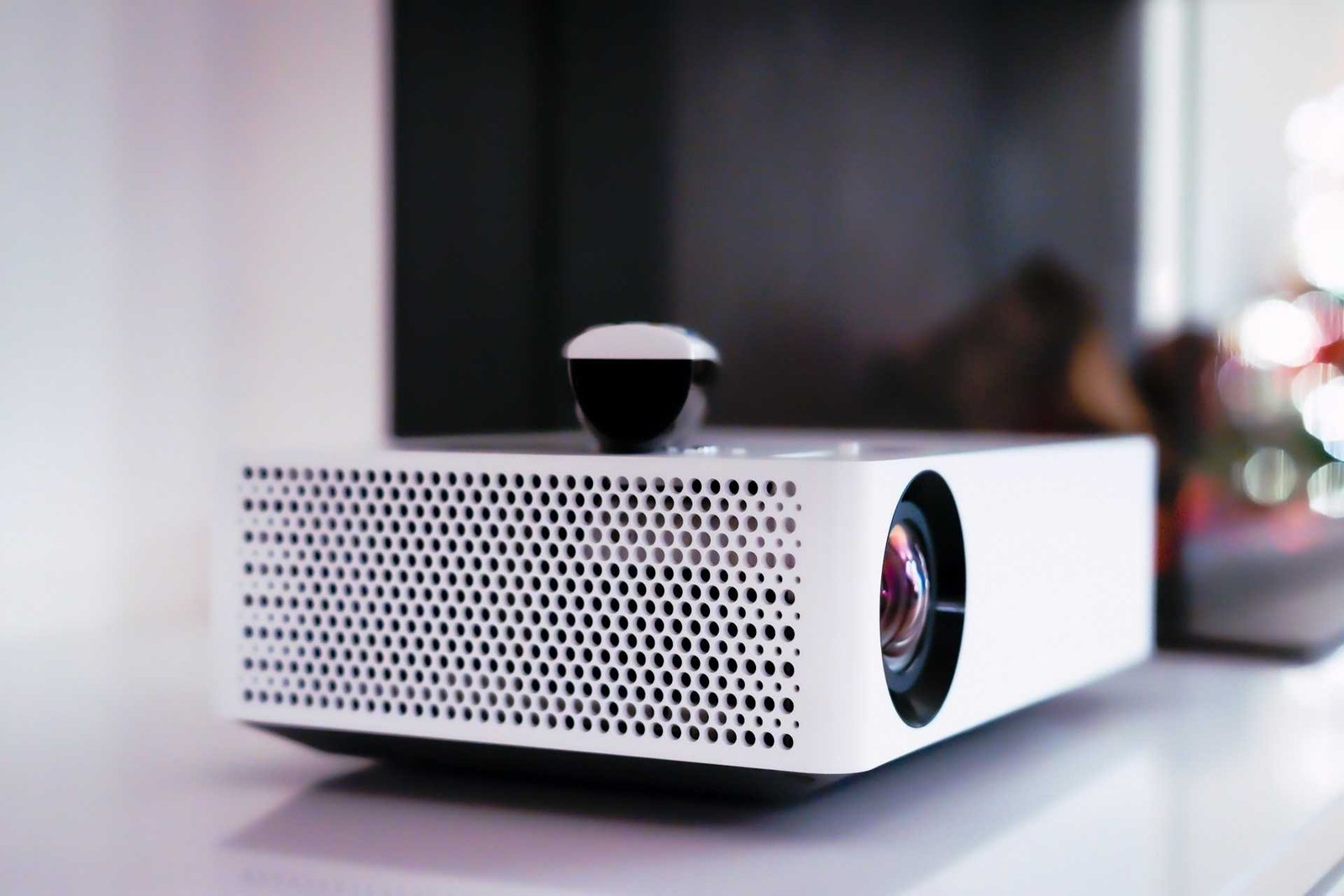 A white mini projector standing on a table next to a TV.
