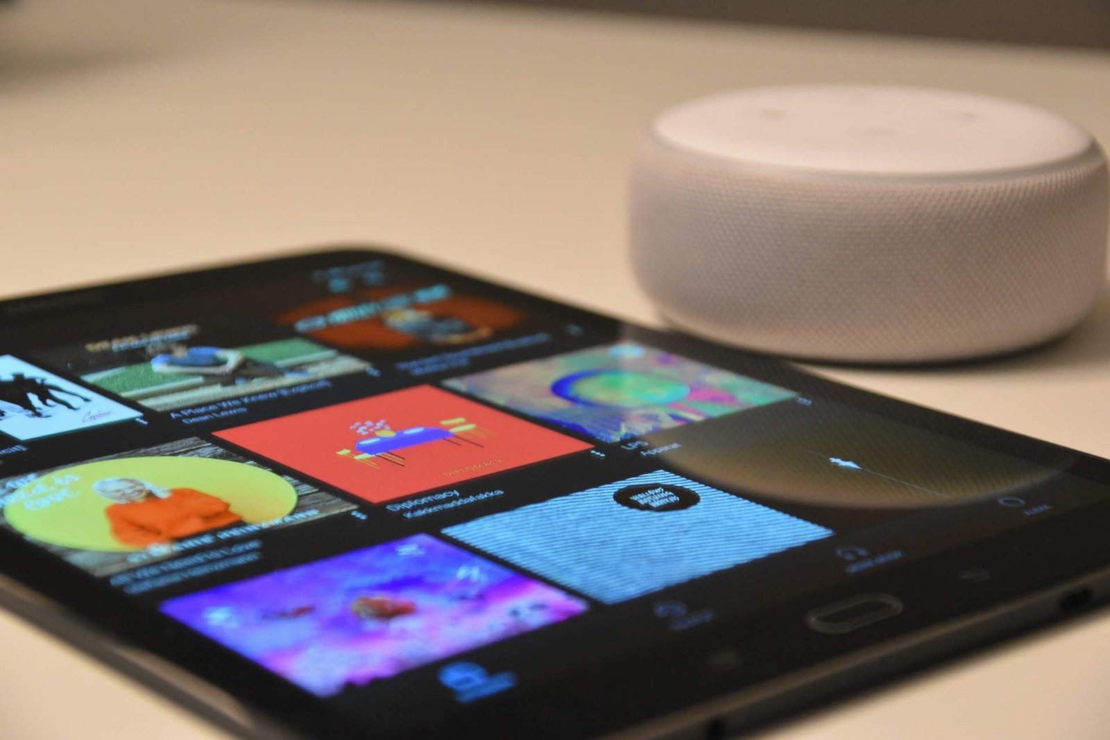 A tablet with music playlists next to a small white speaker.