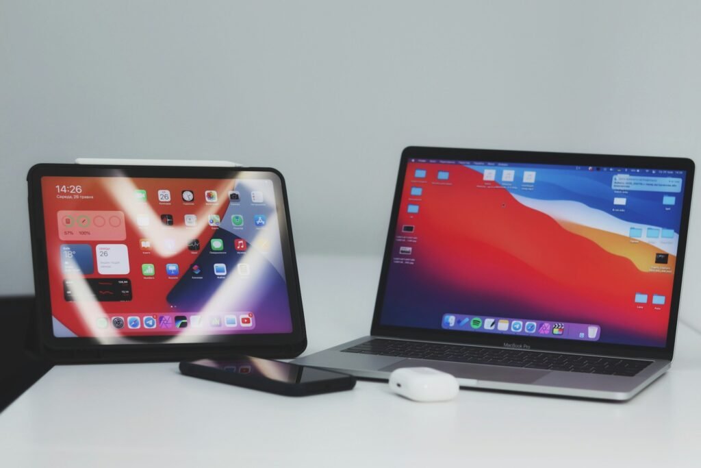 A macbook, ipad smartphone and airpods next to each other.