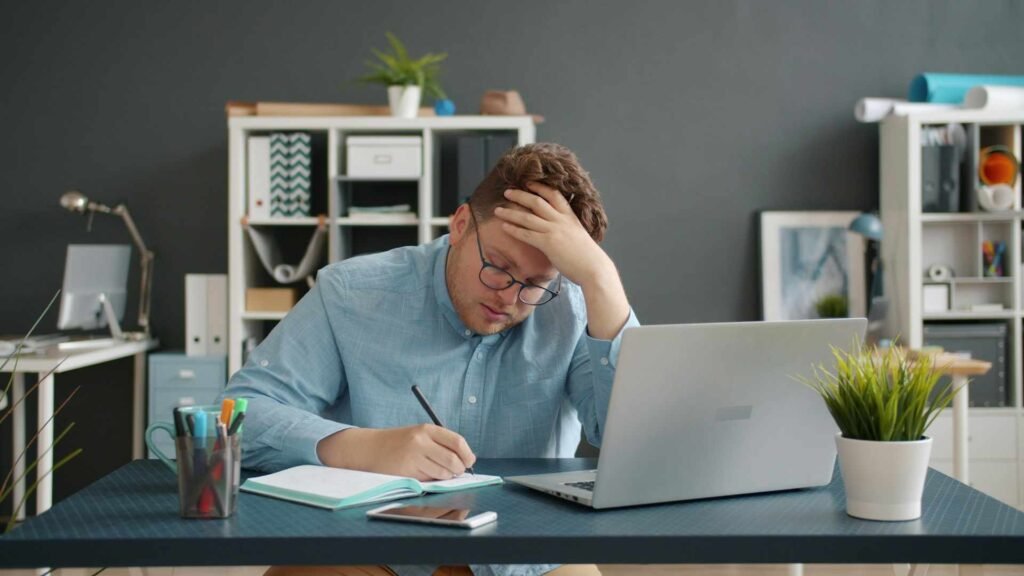 A man sitting and taking notes at an office desk with bad posture.