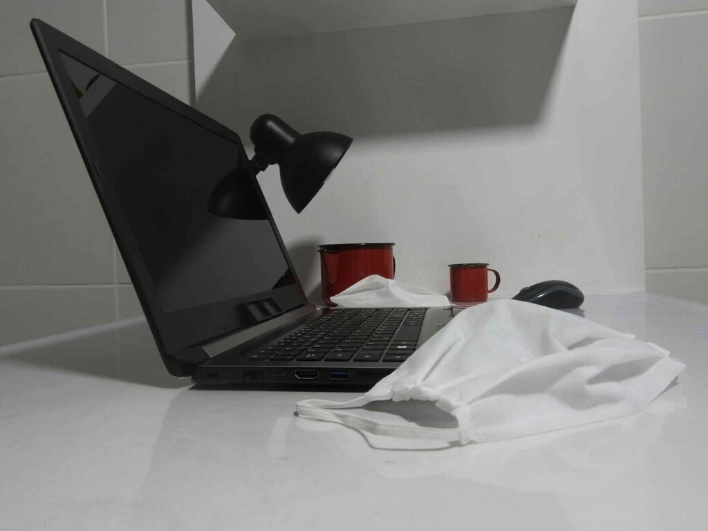 A turned off black laptop on a white table next to a black lamp.