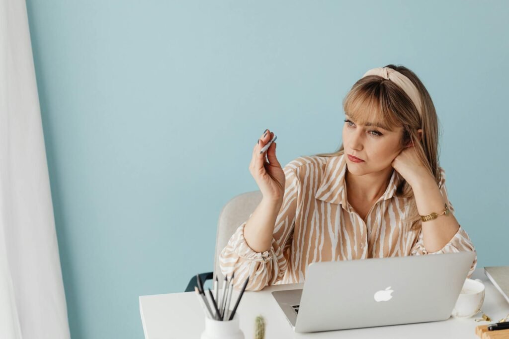 A woman at work with pen in her hand looking out of window while thinking.