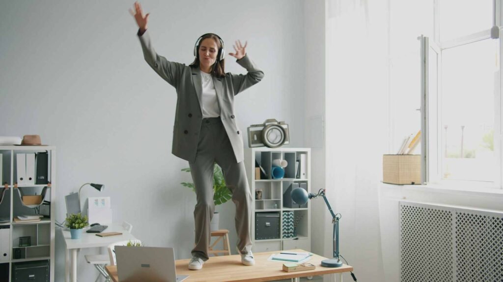 A woman in a suit dancing on a desk at work being distracted by music.