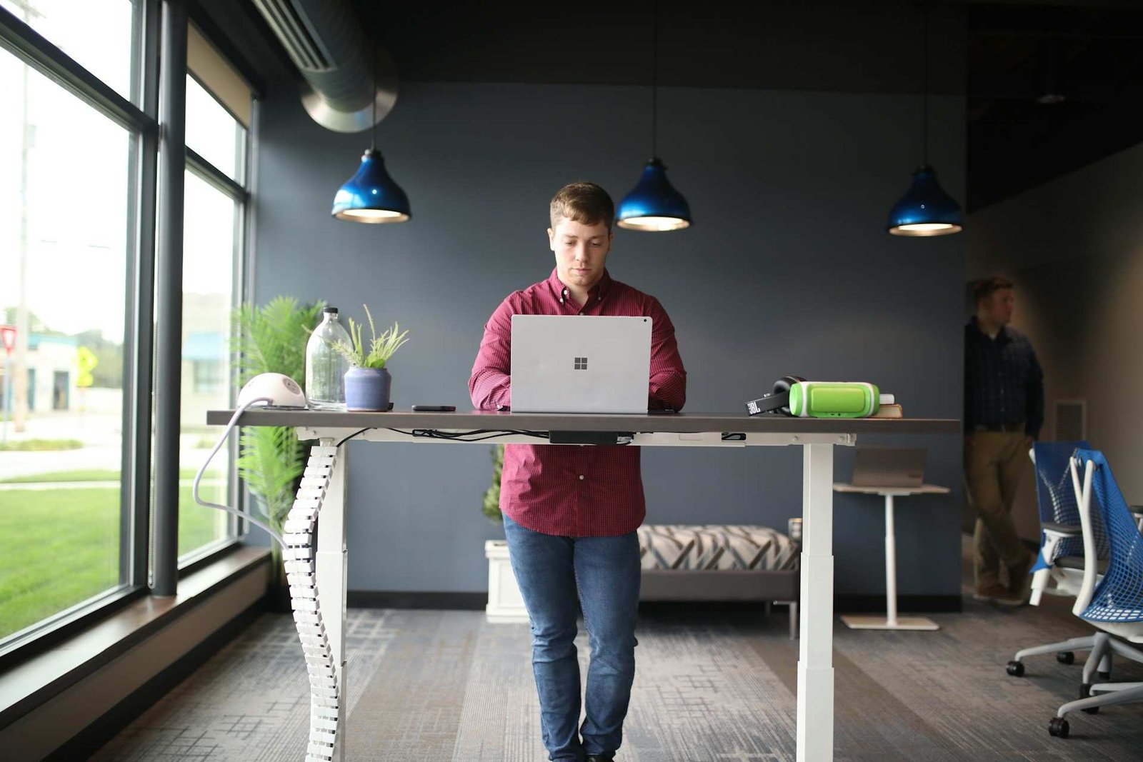 A man in a red shirt working at a standing desk in the middle of the room.