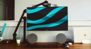 A monitor on a desk mount with two speakers below.