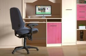 A black chair with a thick armrest in front of a workspace setup at home.