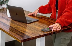 A person in red clothes in front of a wooden rectangular office desk with a laptop on it.