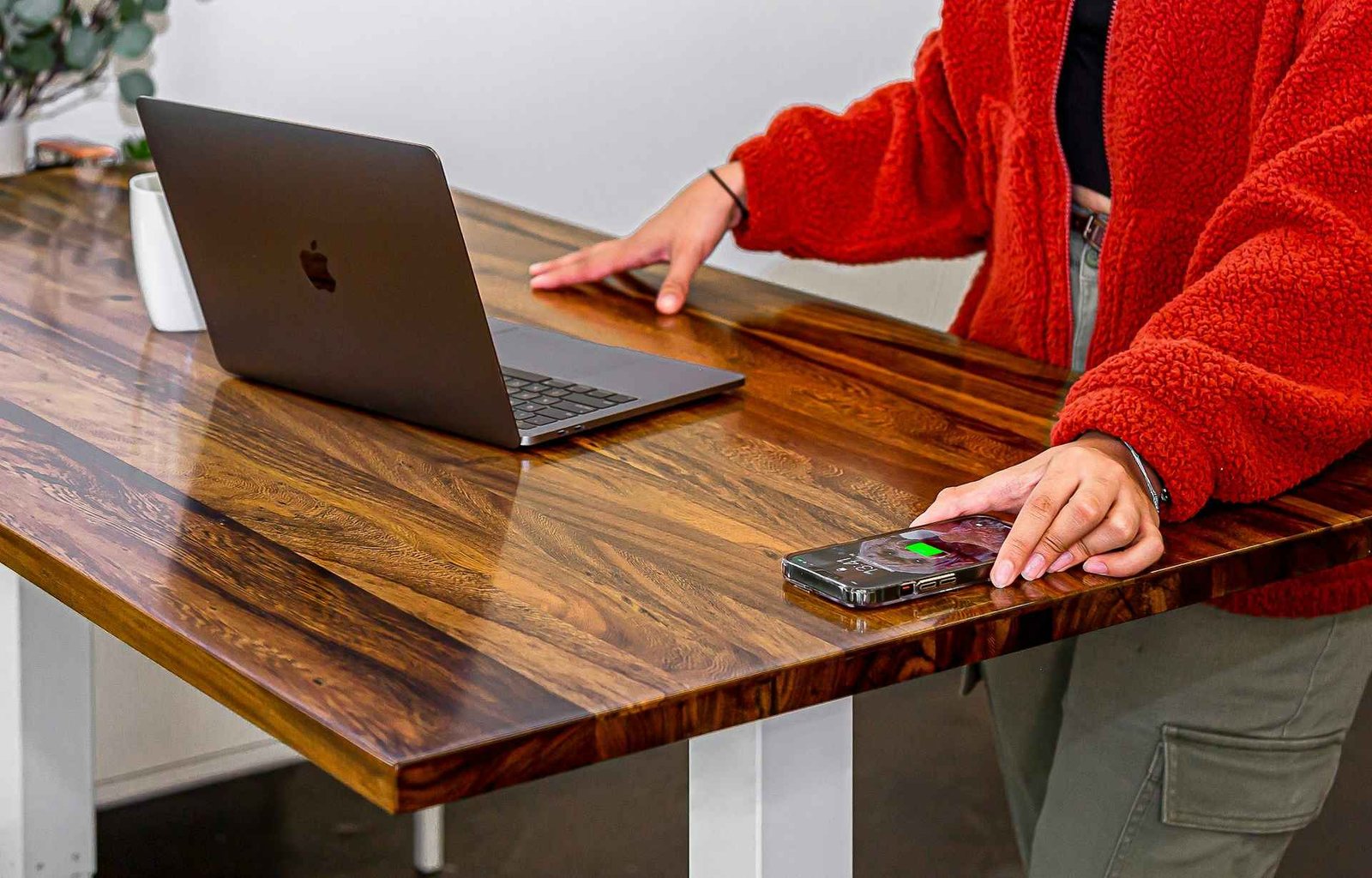 A person in red clothes in front of a wooden rectangular office desk with a laptop on it.