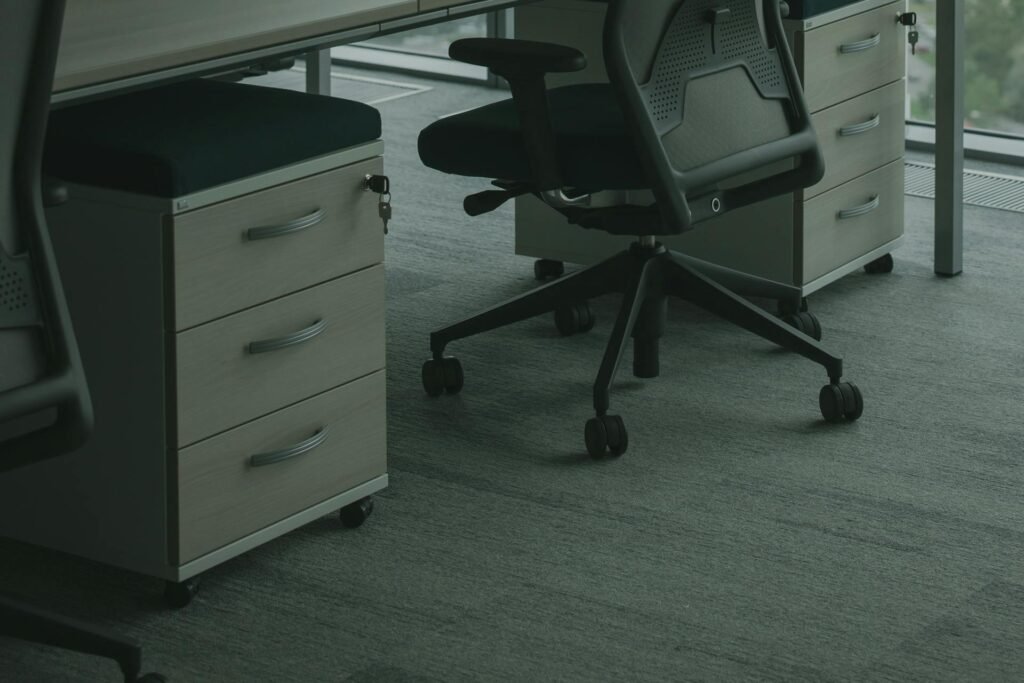A close up of black office chair wheels on a dark carpet.