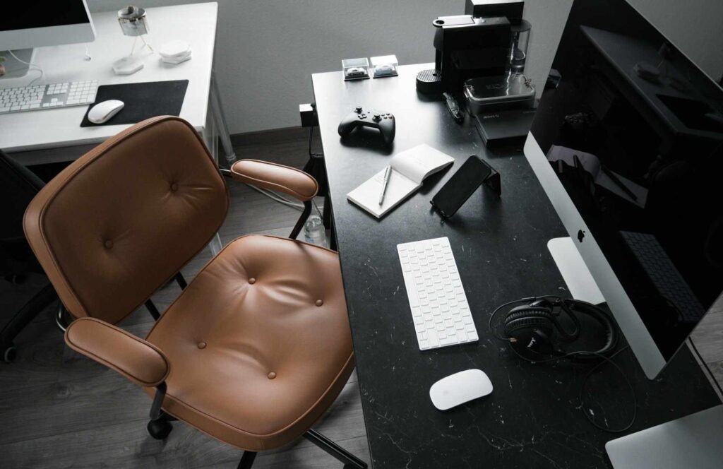 A leather office chair in front of a black table with a work setup.