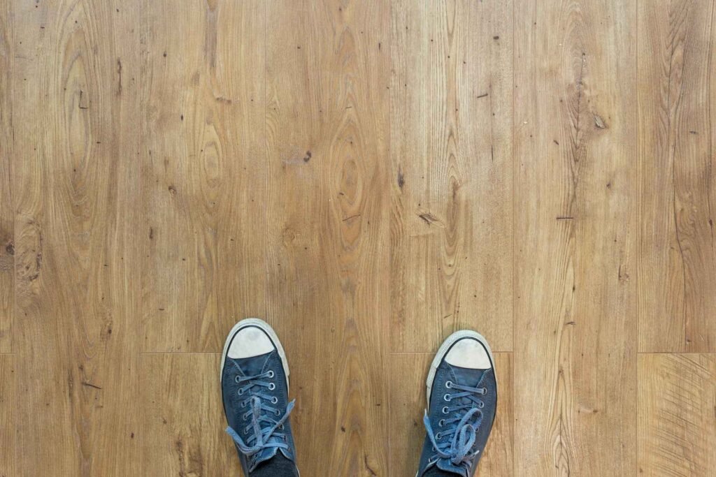 A person in blue and white sneakers standing on a hard wood floor.