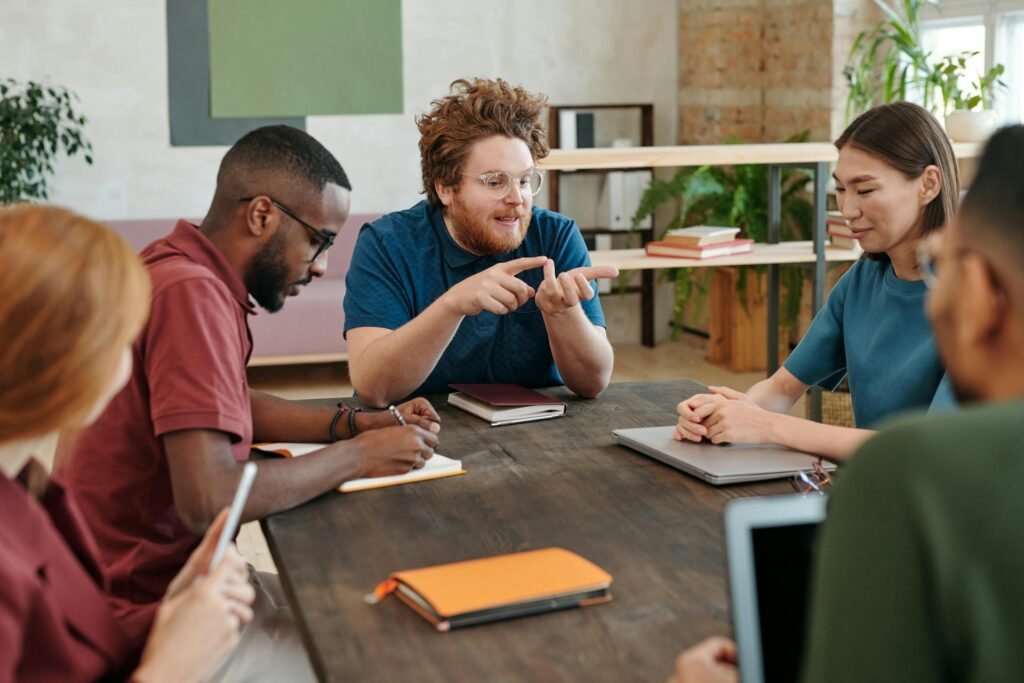 A group of 5 people sitting together and talking at work.