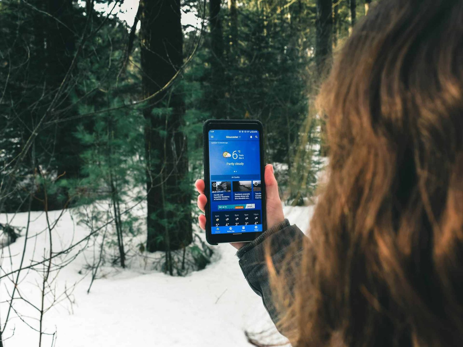 A woman checking the weather on a phone outside around some snow.