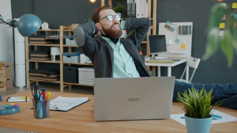 A man relaxing and leaning back in an office chair with his feet on the desk.