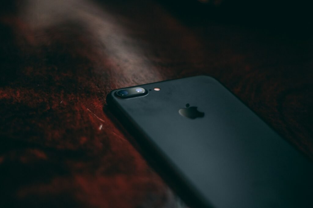A black iphone lying on a wooden desk.