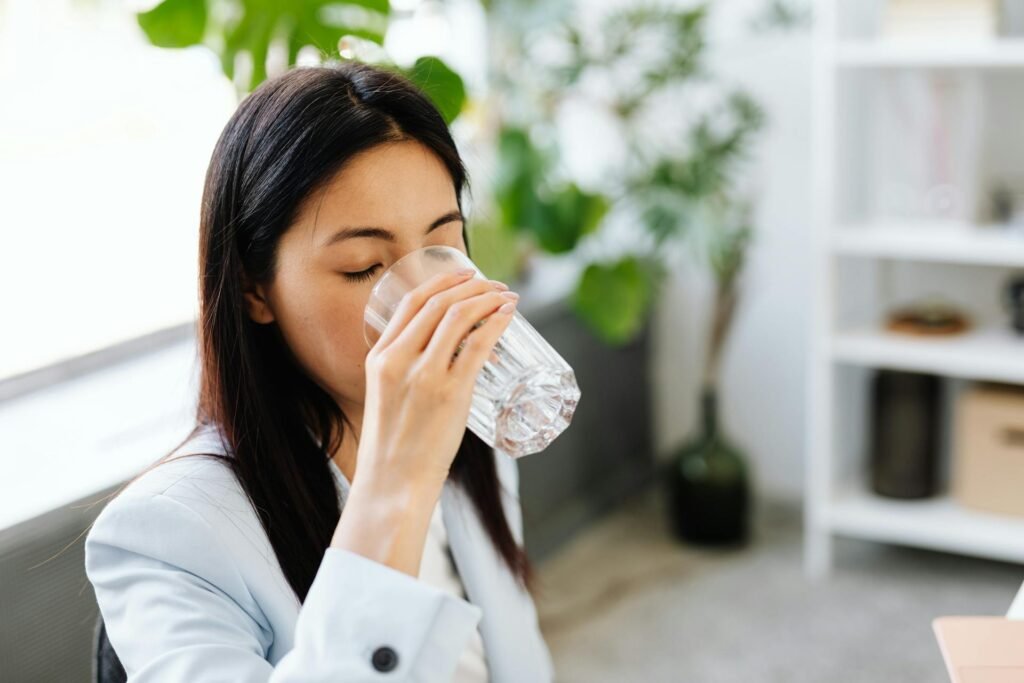 A woman at work drinking water out of a glass.