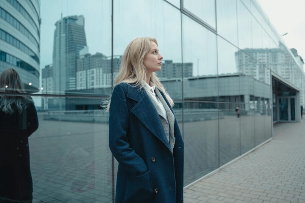 A woman in a blue coat standing in front of a glass building.