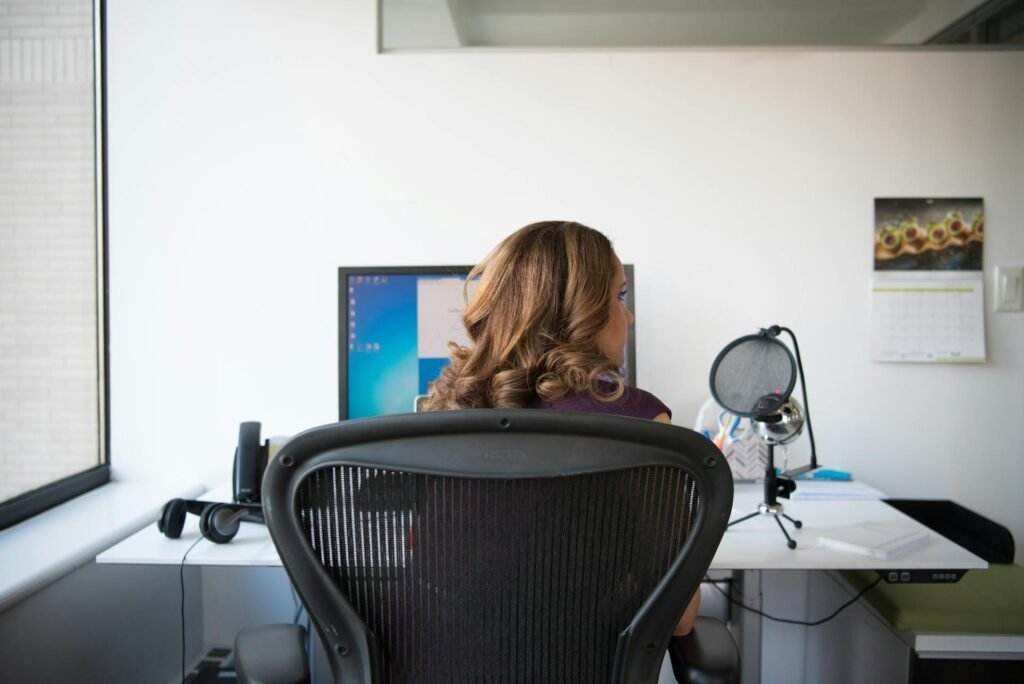 A woman sitting one sided on an office chair in front of a computer