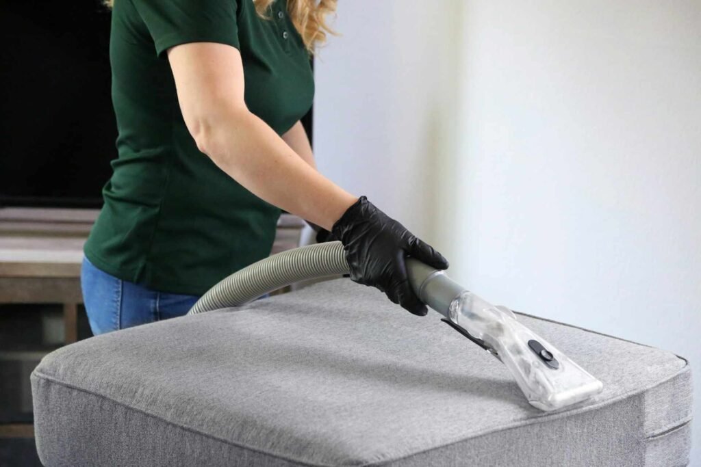 A woman vacuuming a grey cushion.