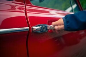 A person opening the car door of a red car.