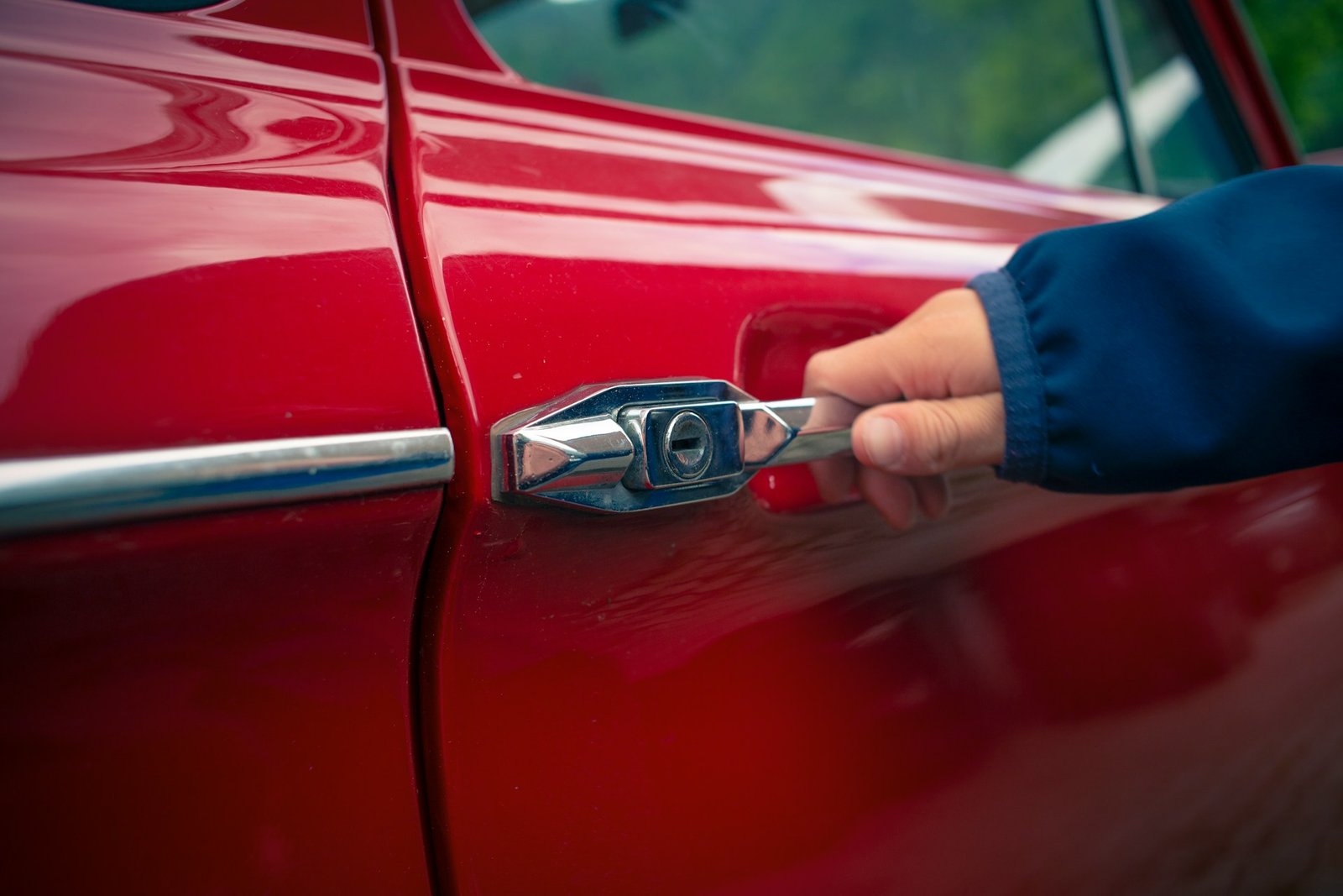 A person opening the car door of a red car.
