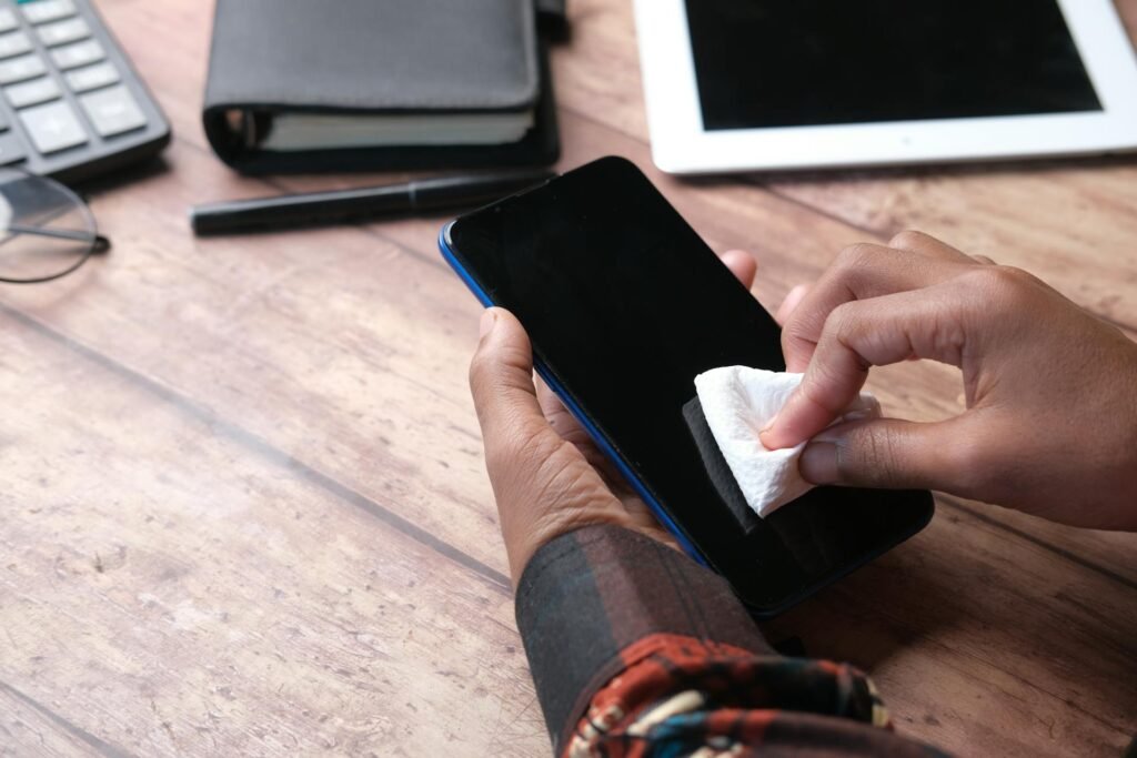 A person cleaning a phone with a paper towel on a wooden desk.