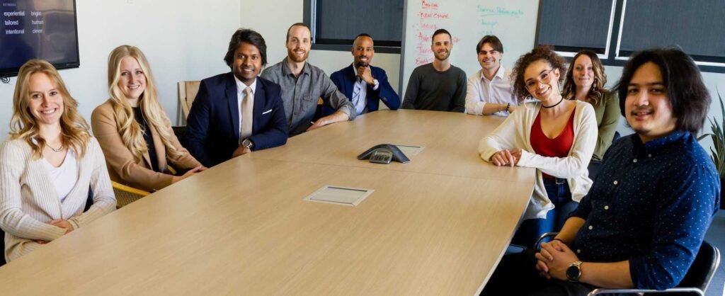 10 people around a long desk in a meeting room looking at the camera or presenter.