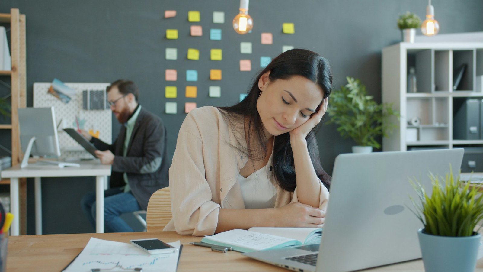 A woman resting her head on her hand and sleeping at work in front of a laptop.