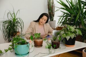 A woman working at a table being surrounded by many different plants.