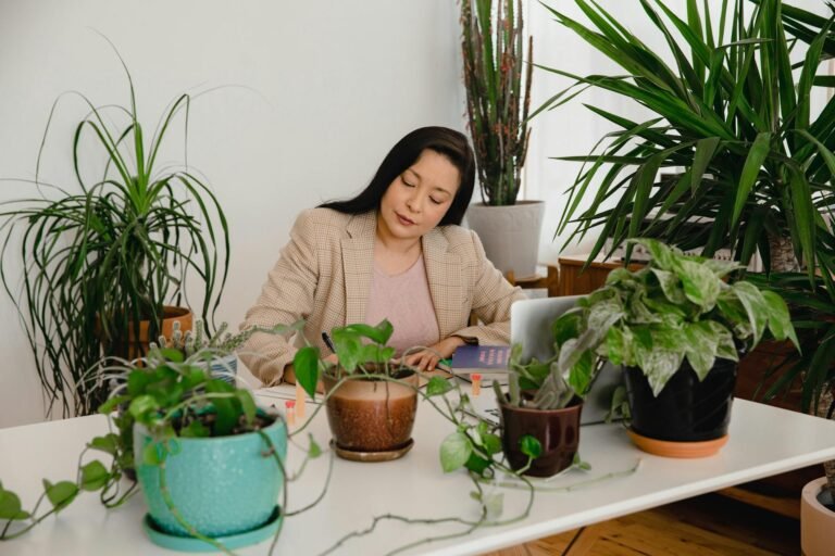 A woman working at a table being surrounded by many different plants.